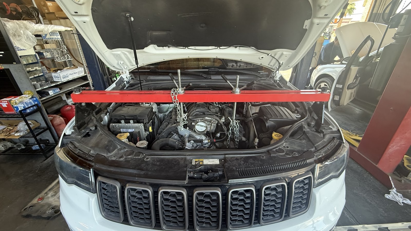 White Jeep Grand Cherokee with hood open and engine support bar installed for engine service