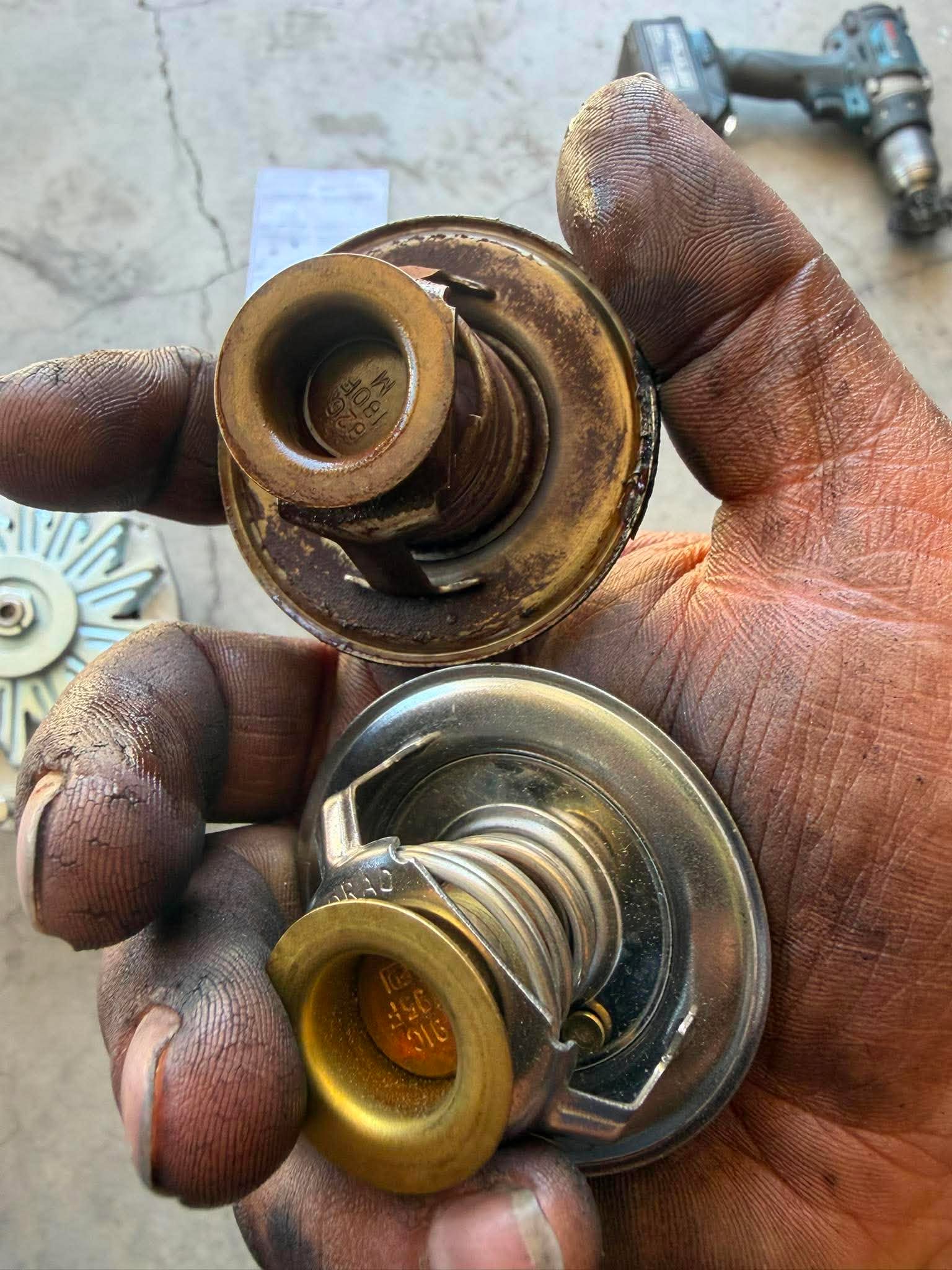 Two thermostats held in hand, showing old rusted unit versus new one