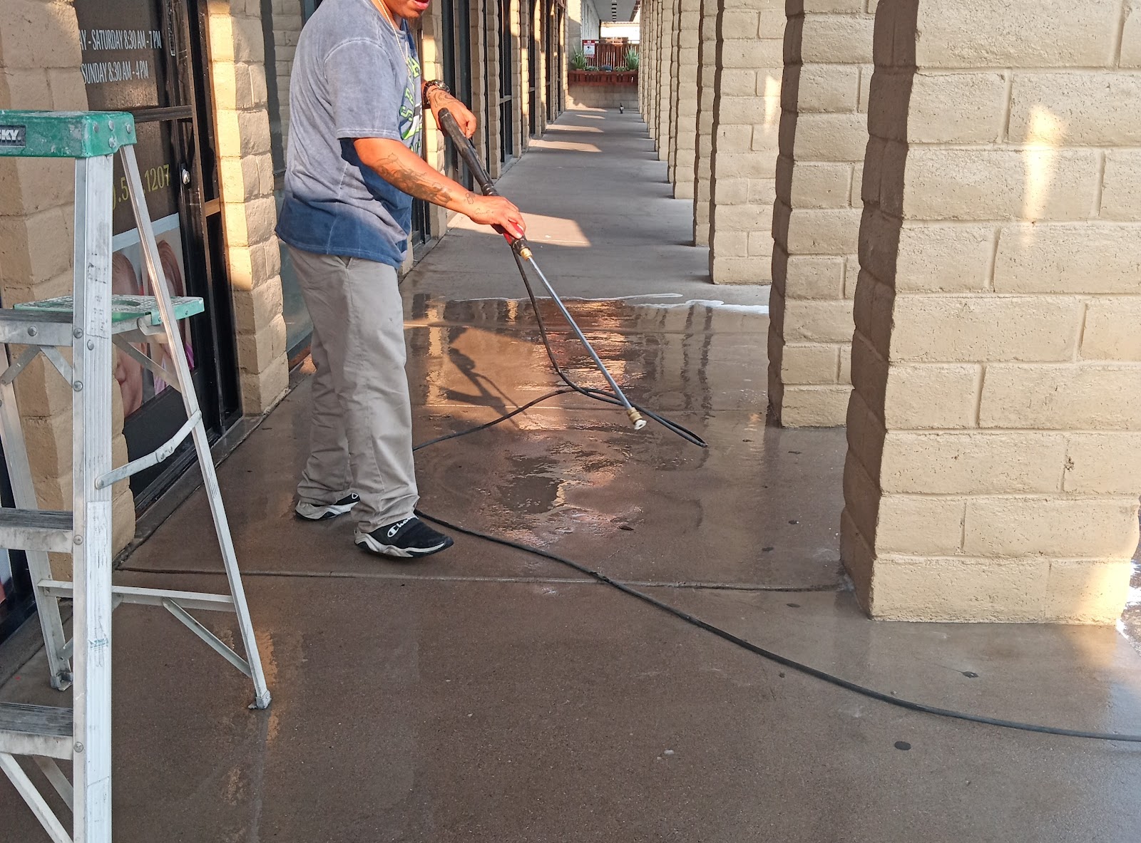 Worker pressure washing wet concrete walkway at a strip mall