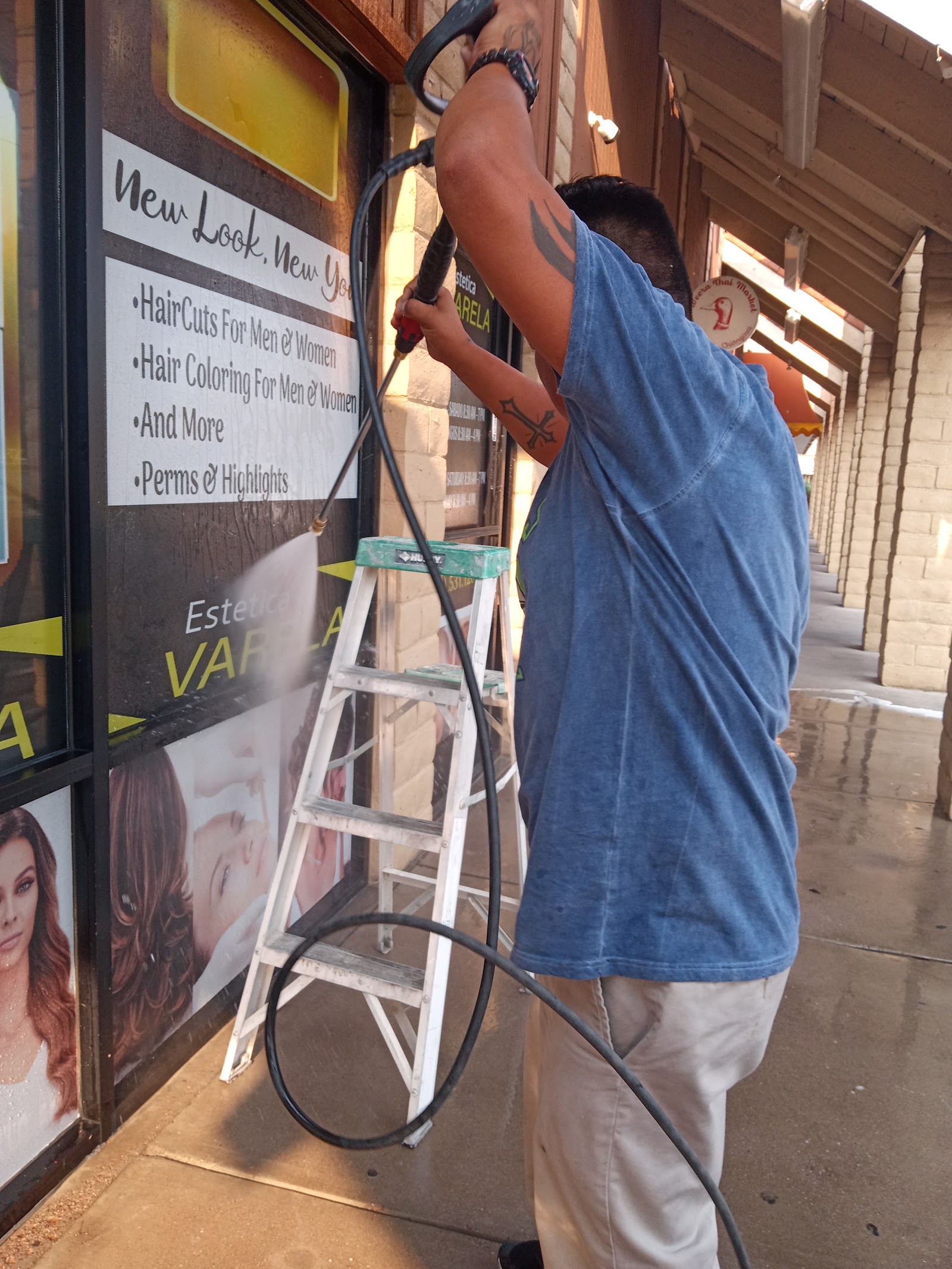 Worker pressure washing storefront window and signage at a strip mall