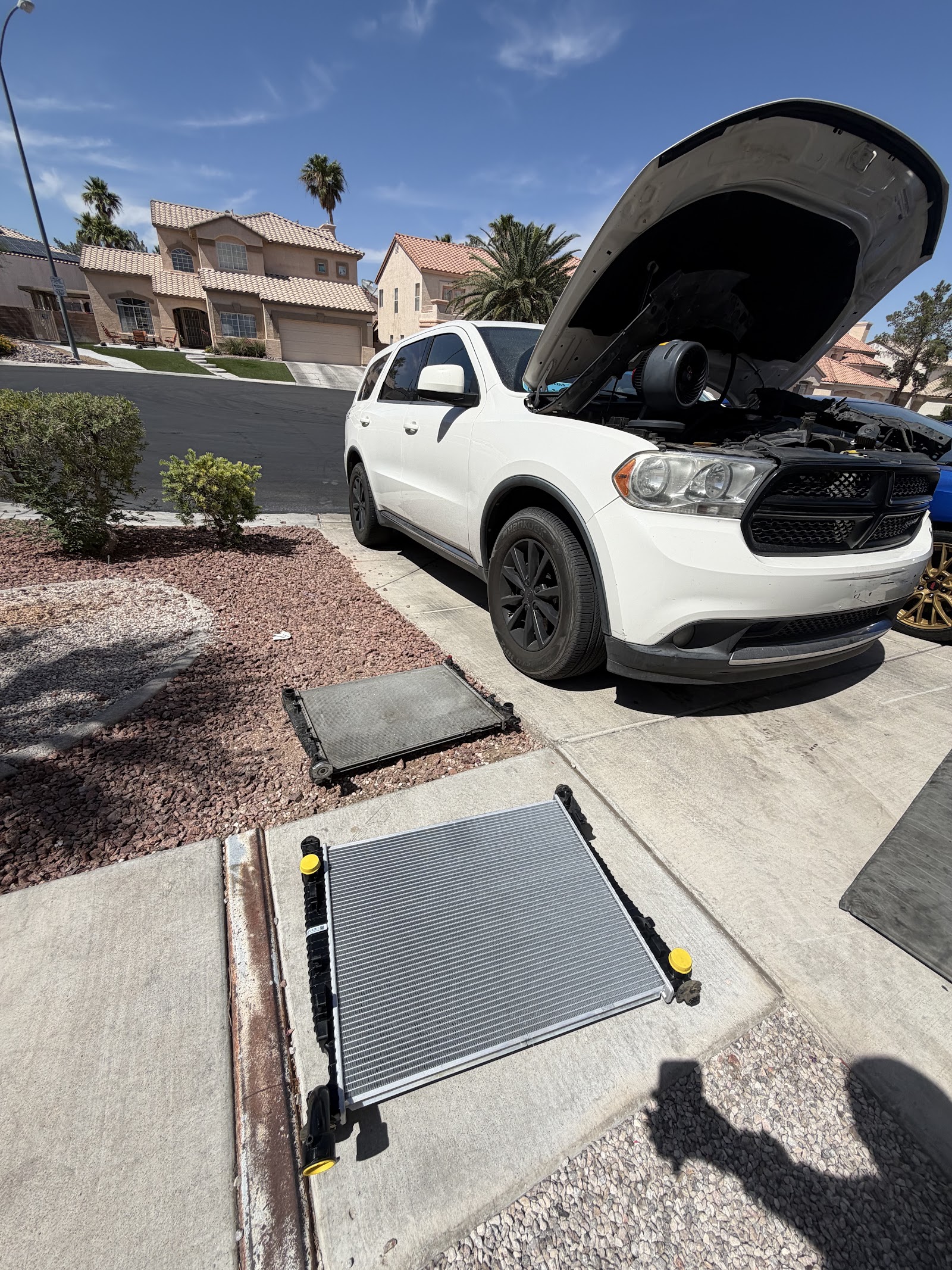 White Dodge Durango with hood up and old and new radiators in driveway