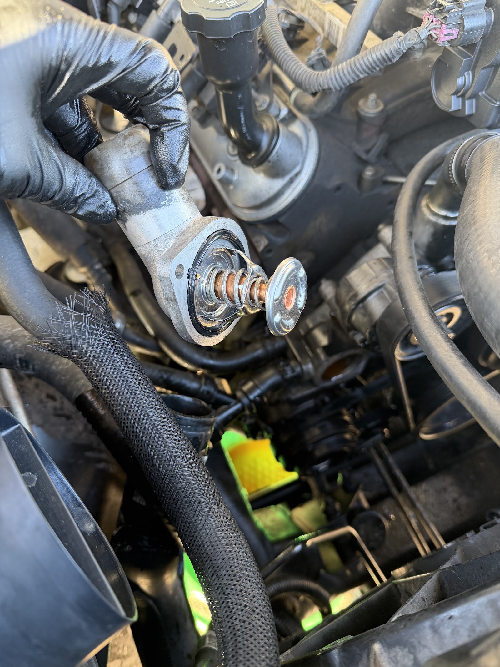 Hand holding thermostat housing during engine coolant service
