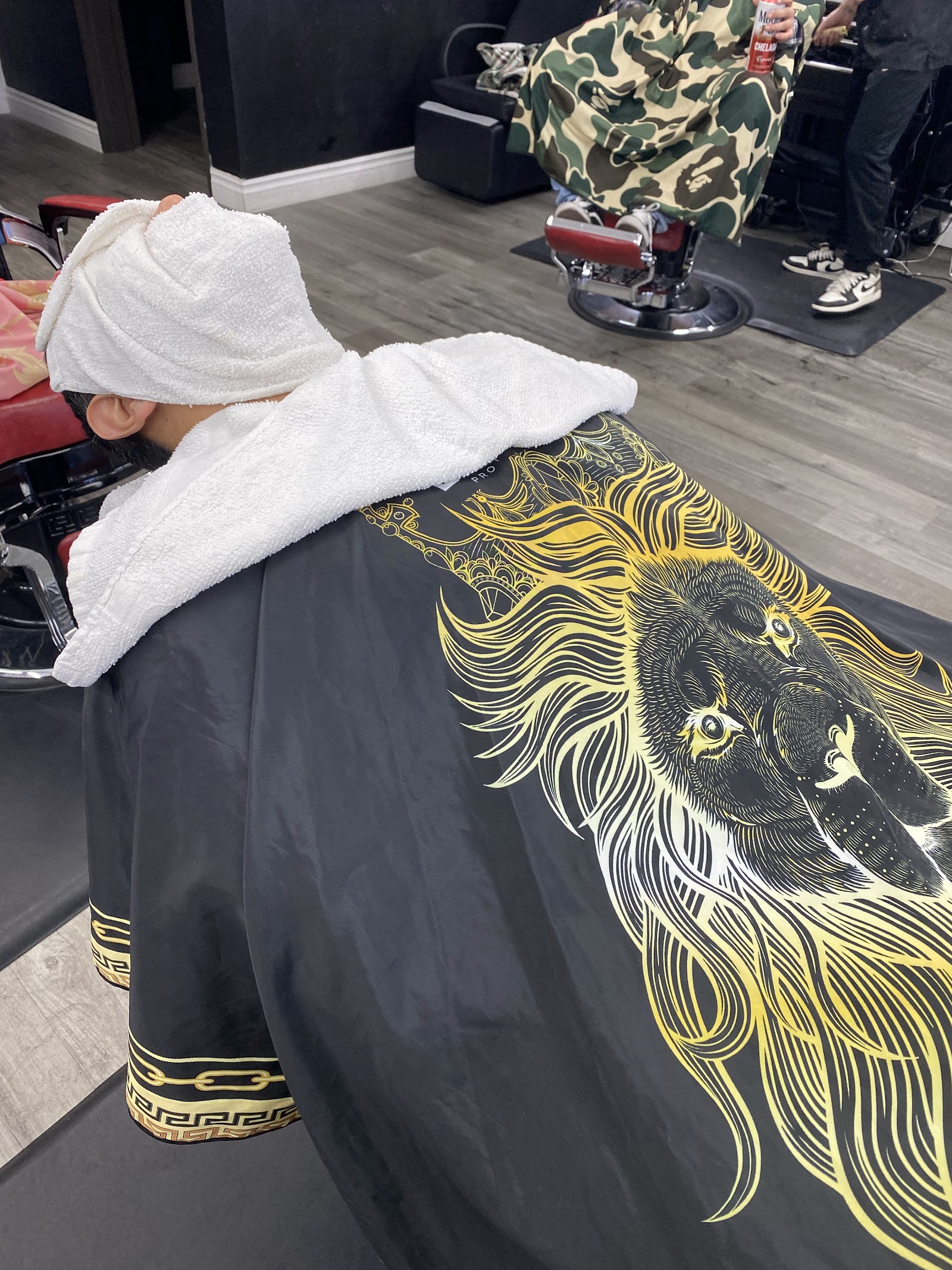 Client reclined with hot towel and lion-print cape during a barbershop service
