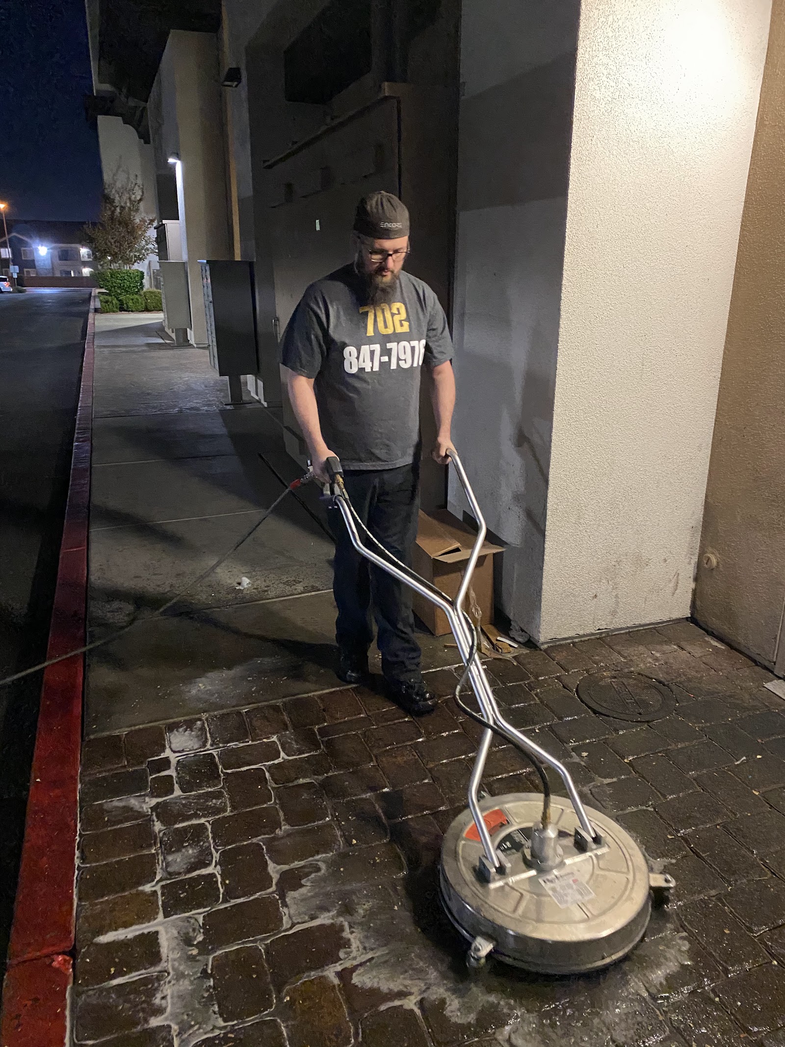 Worker in branded 702 shirt using surface cleaner on paver walkway at night