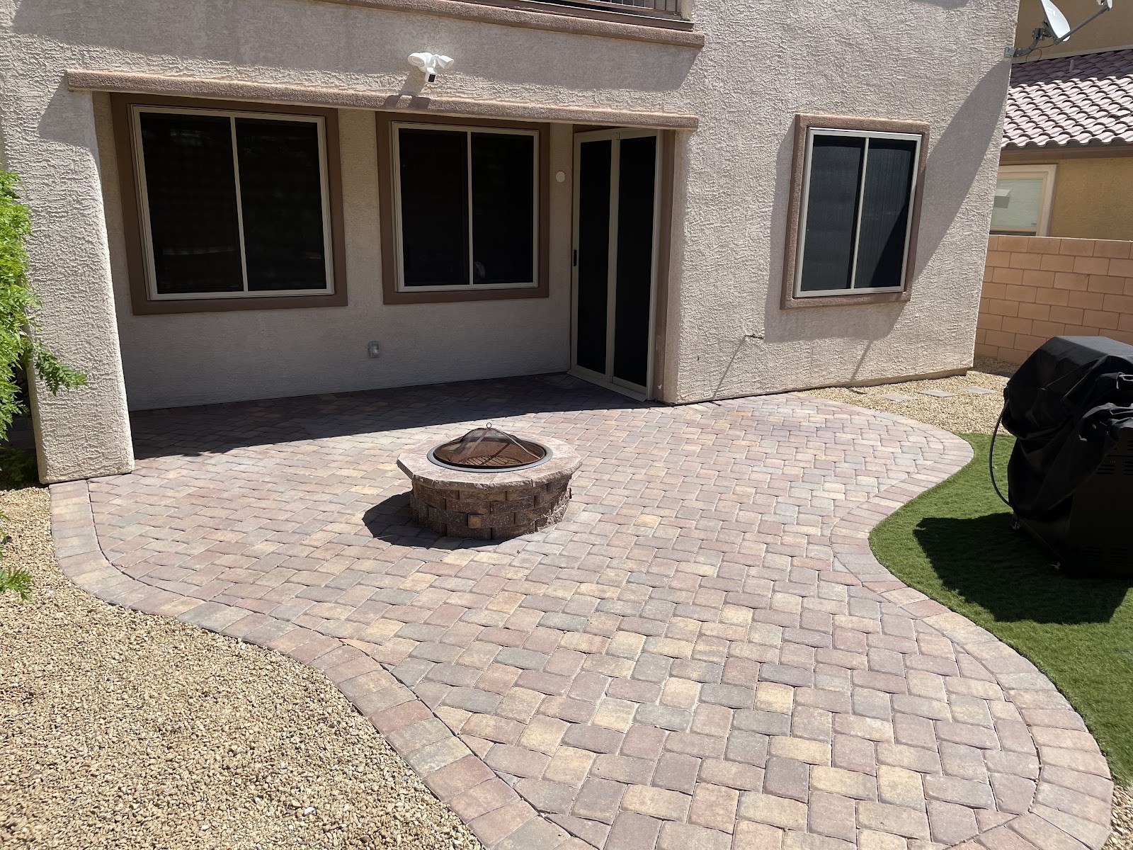 Clean paver patio with fire pit behind a home backyard