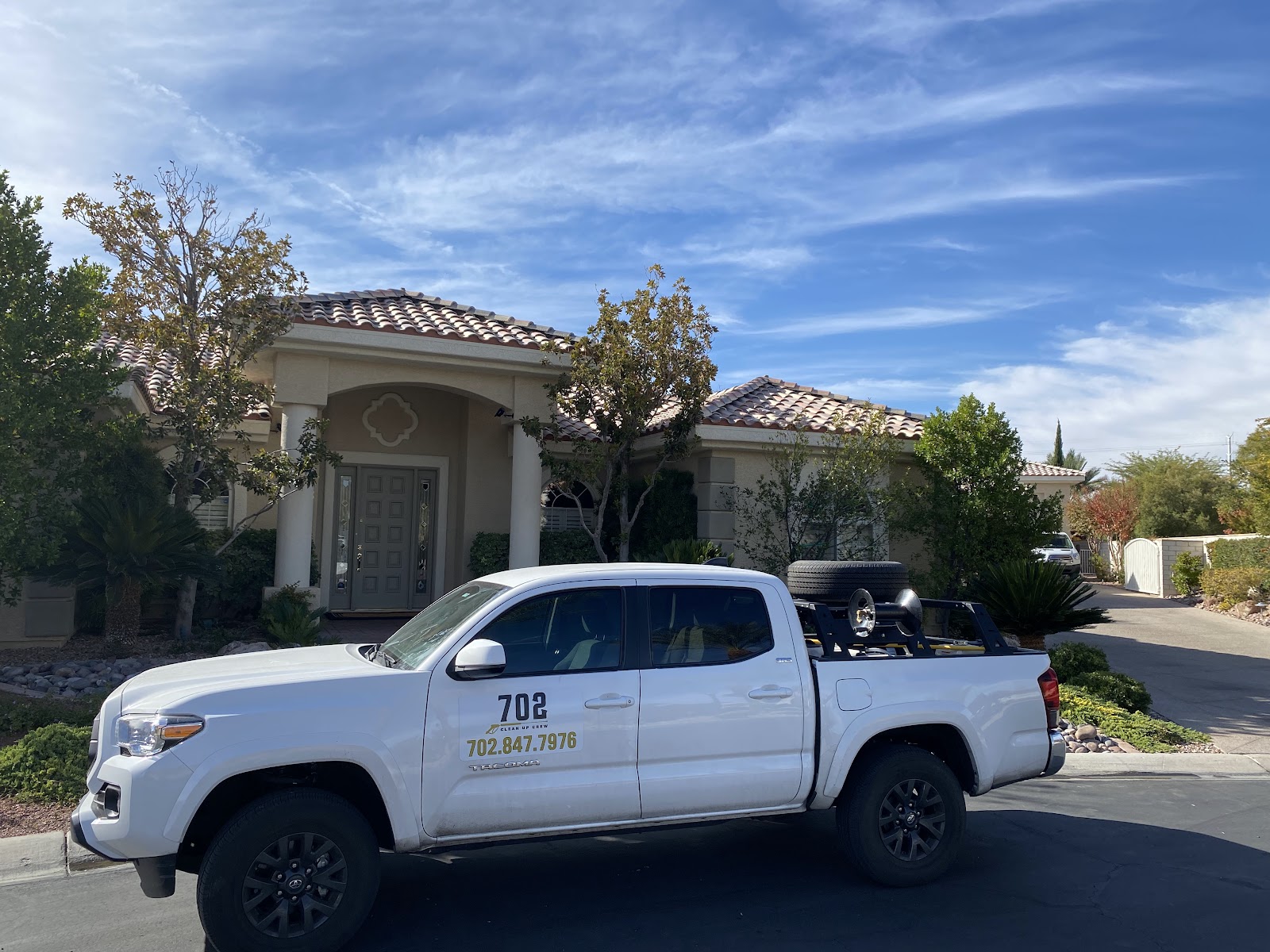 White Toyota Tacoma with 702 branding and equipment parked in front of home under blue sky