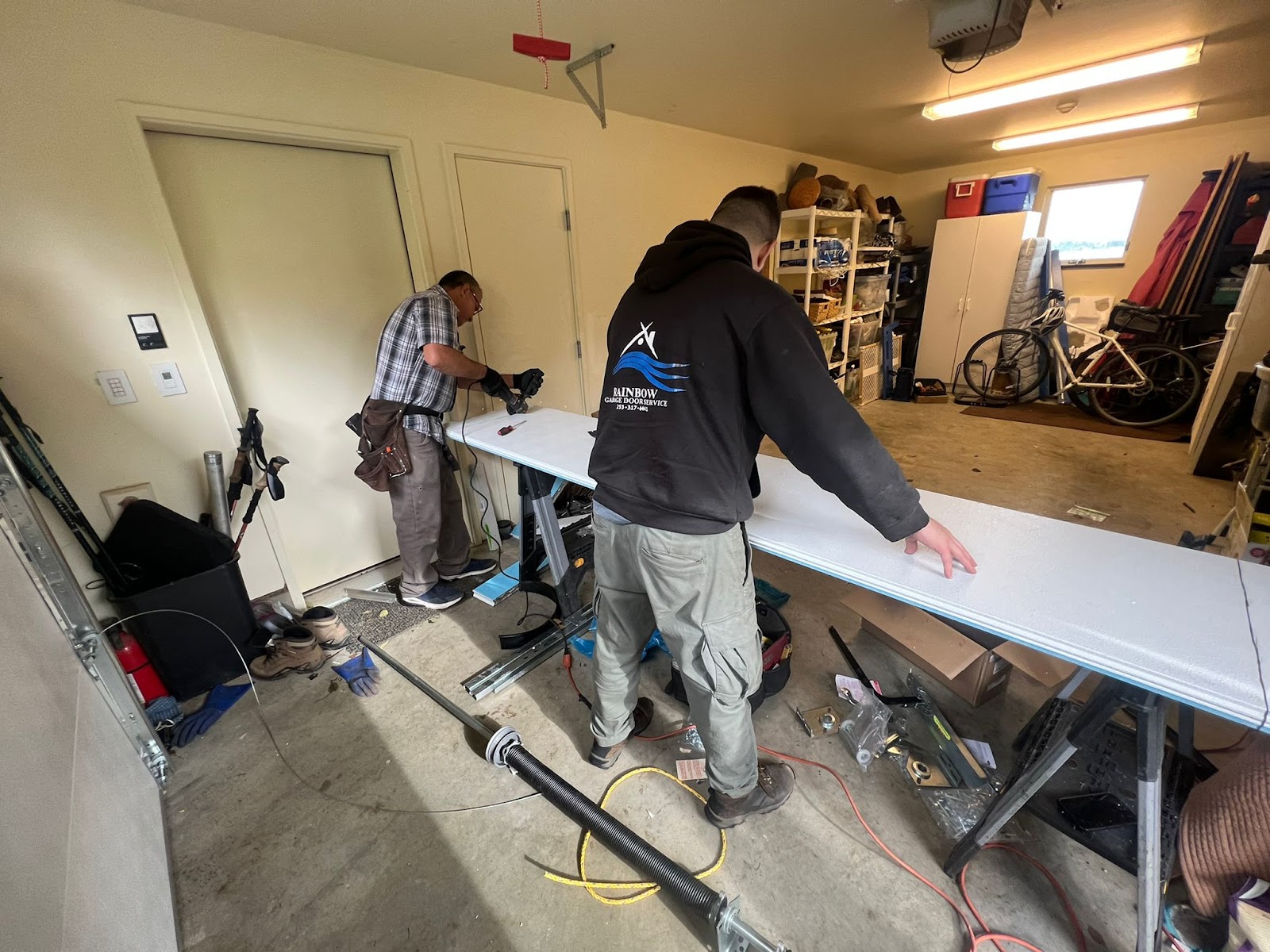 Two Rainbow Garage Door technicians working on garage door panel in a residential garage