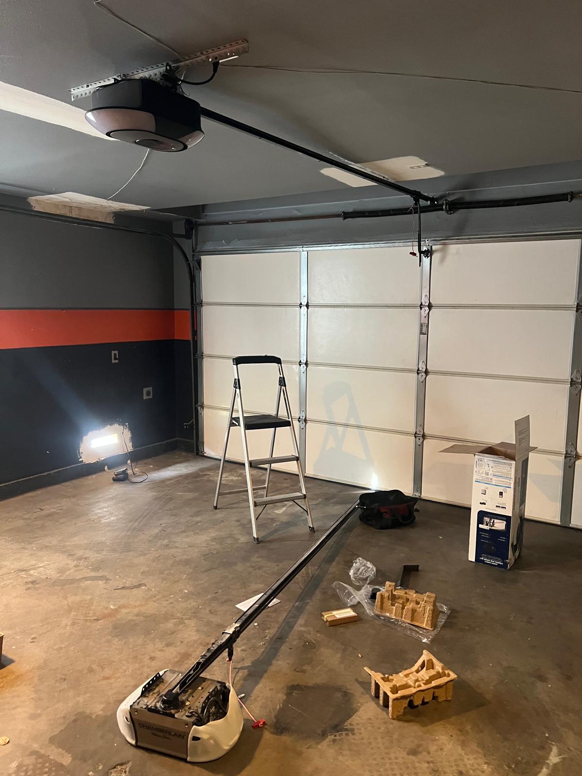Garage door opener installation in progress with ladder, rail and old opener on floor