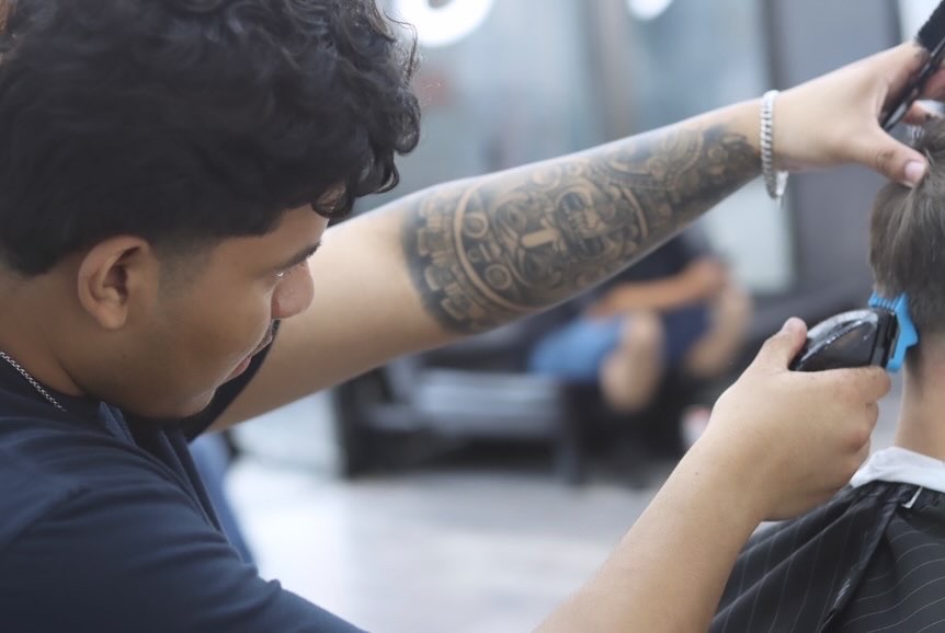 Barber with tattooed forearm cutting a client's hair with clippers