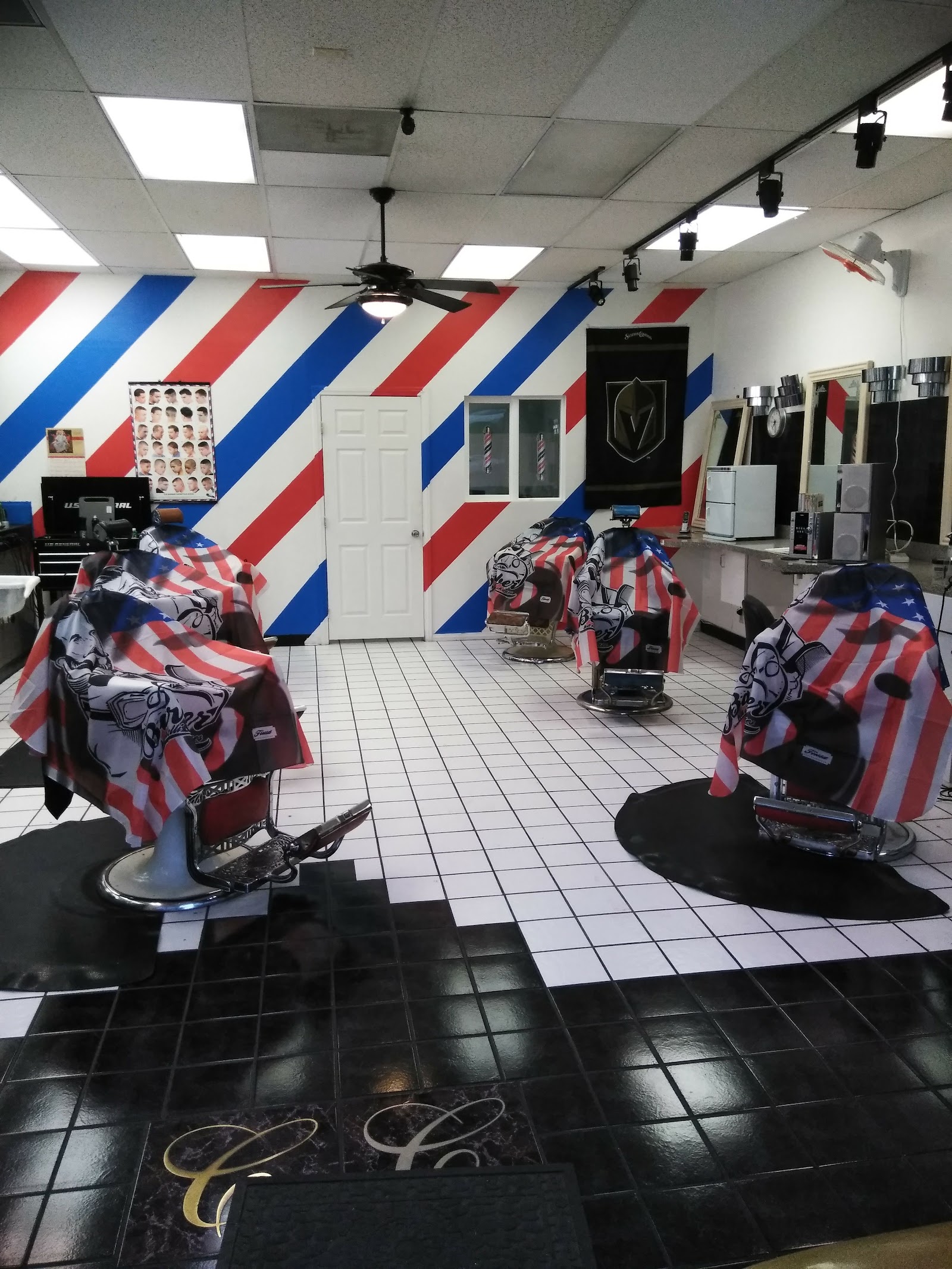Interior of barbershop with red white and blue striped walls, barber chairs draped with American flag capes, and checkered floor
