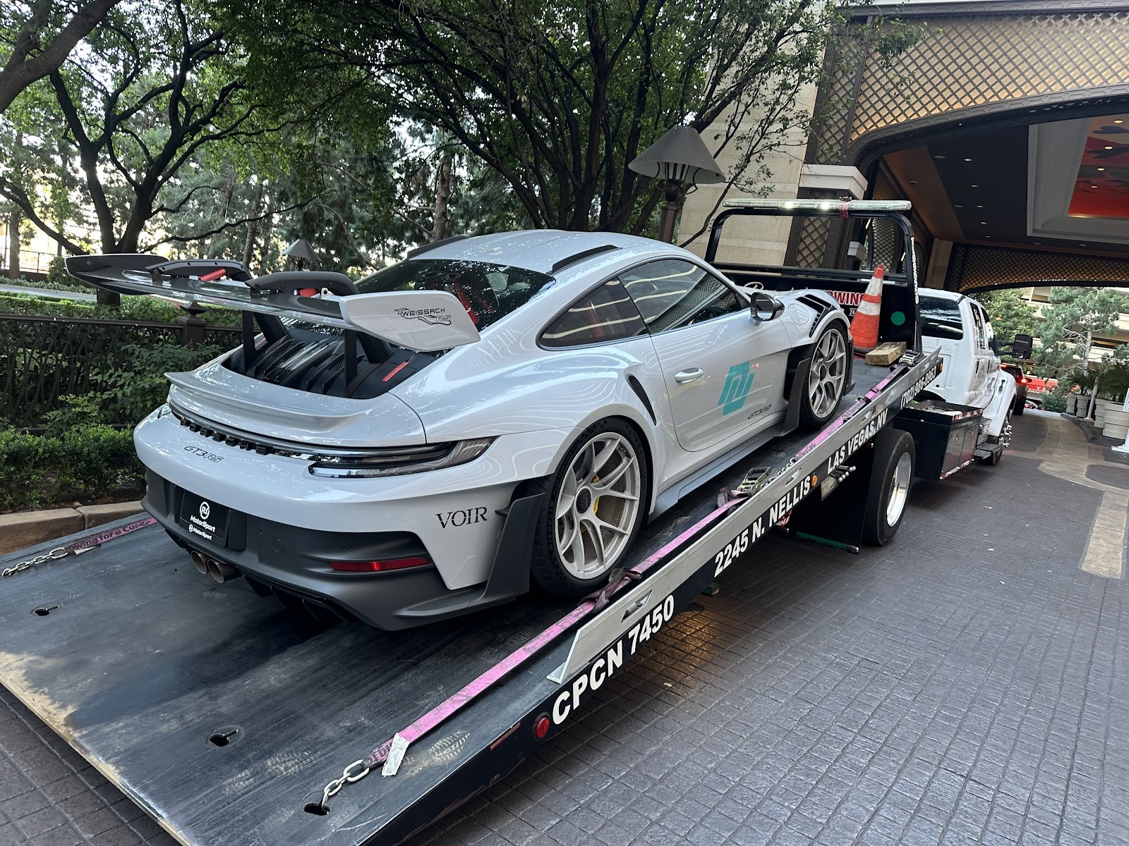 White Porsche 911 GT3 RS with rear wing loaded on a Reggie's Towing flatbed at a resort entrance