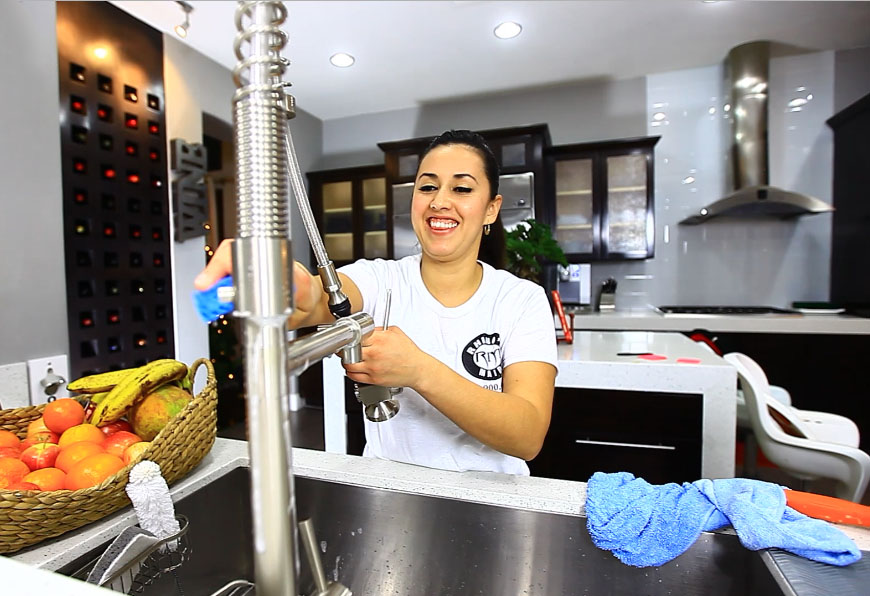 Smiling Rhino's Maid employee cleaning a kitchen sink faucet