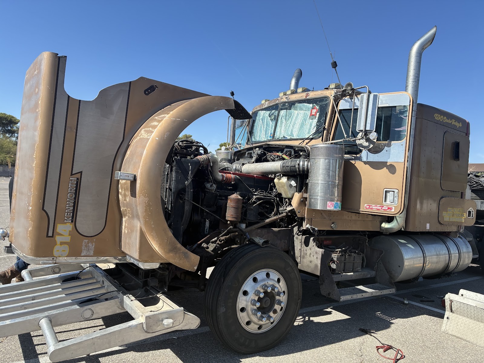 Kenworth semi truck with hood open exposing engine during roadside repair in daylight