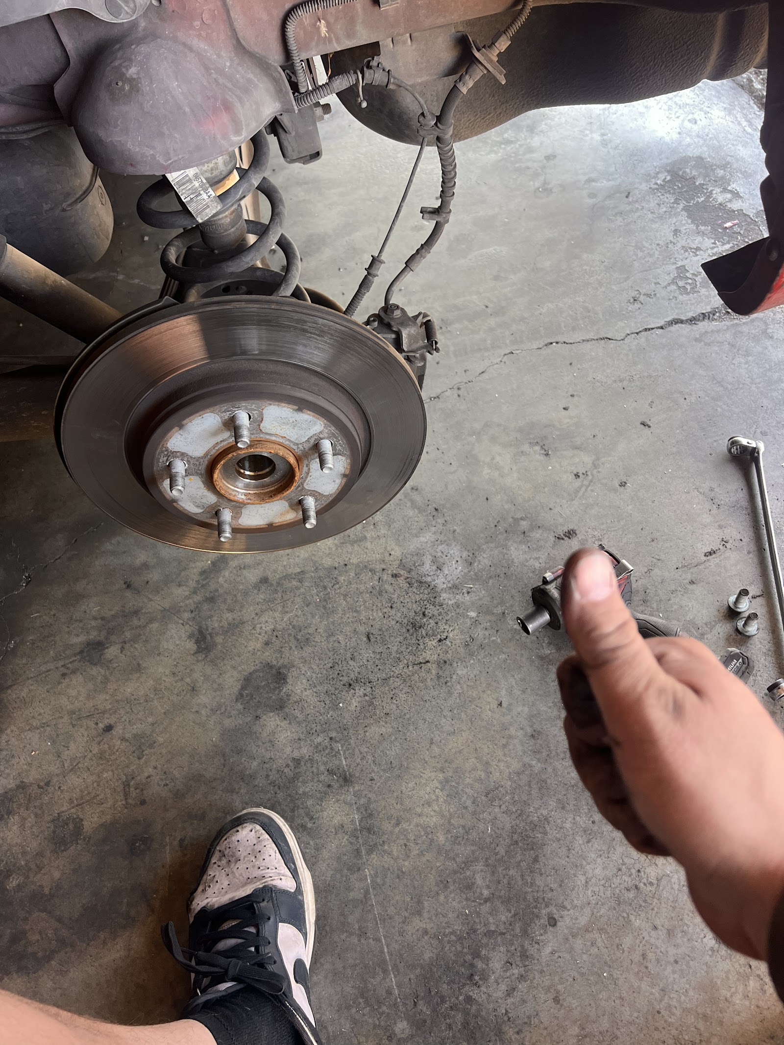 Mechanic holding removed suspension component next to exposed rear brake rotor and hub