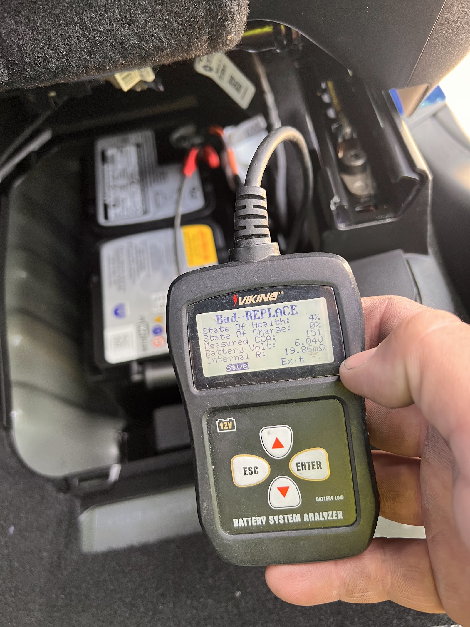 Battery analyzer displaying 'Bad-REPLACE' result held near vehicle battery