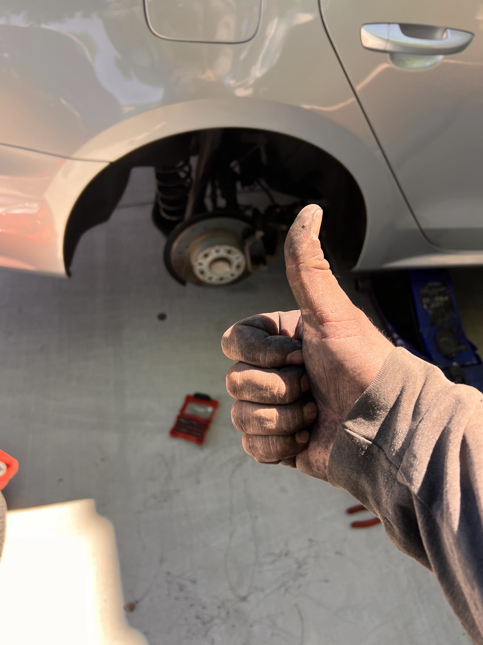 Mechanic's dirty hand giving thumbs up next to a car with wheel removed