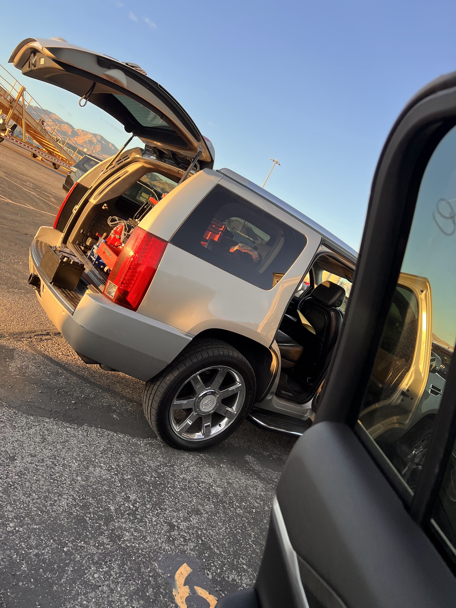 Cadillac Escalade with rear hatch open loaded with tools at sunset in a parking lot