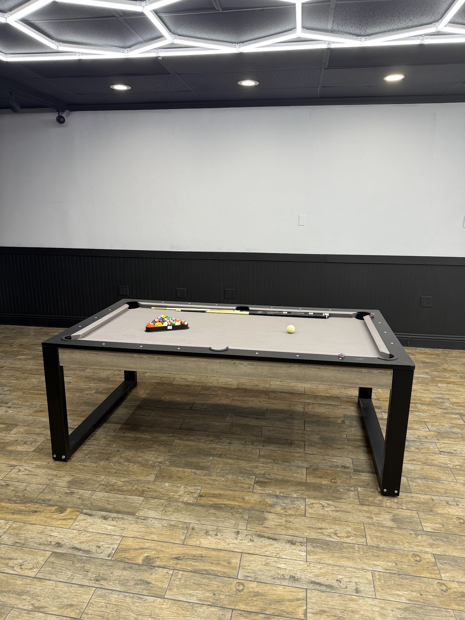 Pool table with balls and cues in barbershop lounge area under hexagonal lights