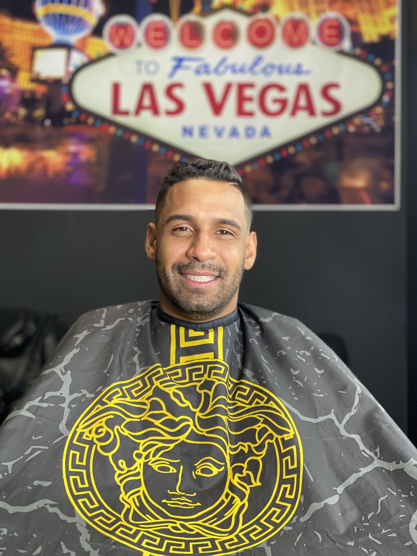 Smiling client with fresh haircut seated in barber chair under Las Vegas sign backdrop