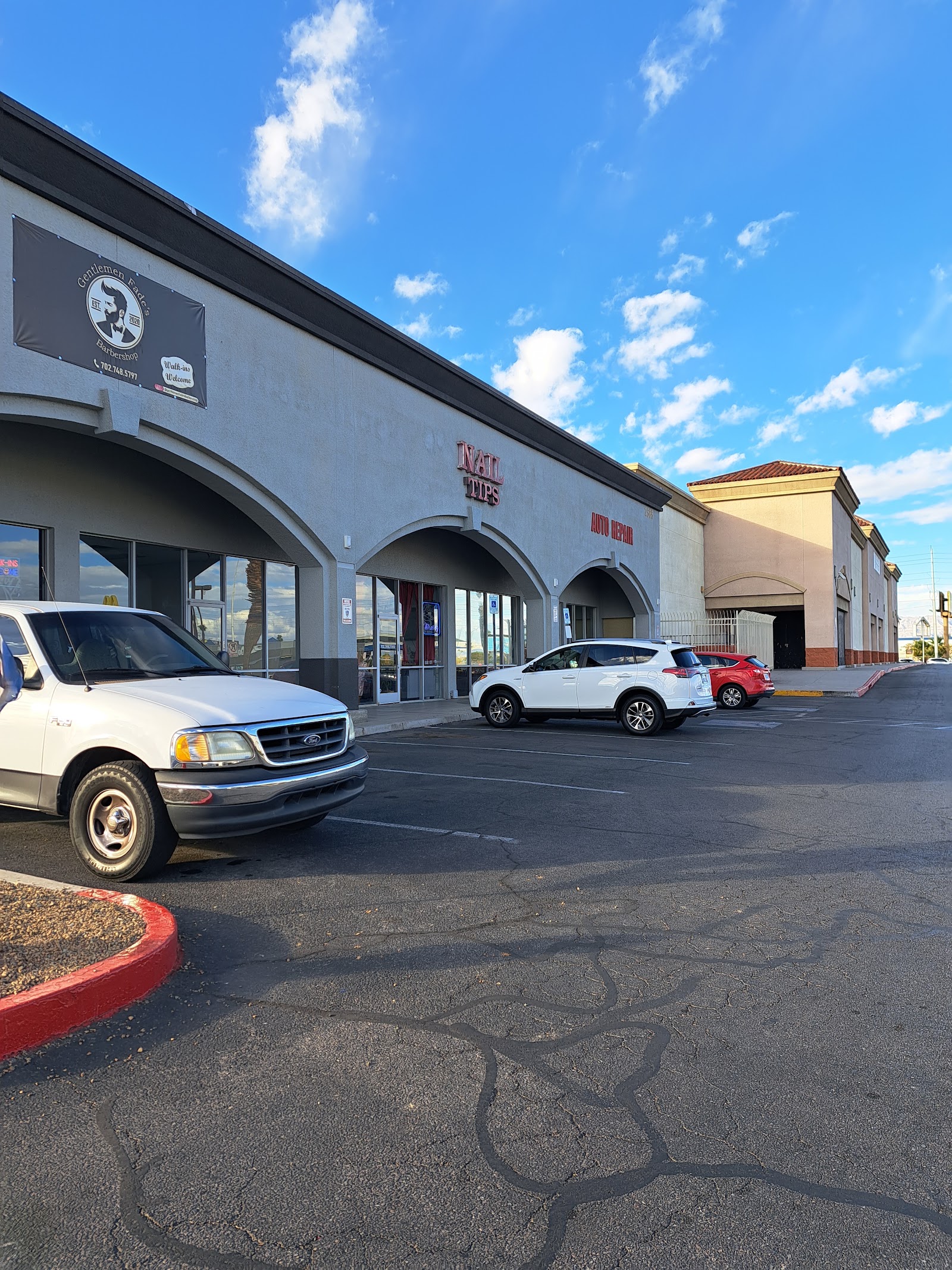 Strip mall exterior showing barbershop with neighboring nail and auto repair shops