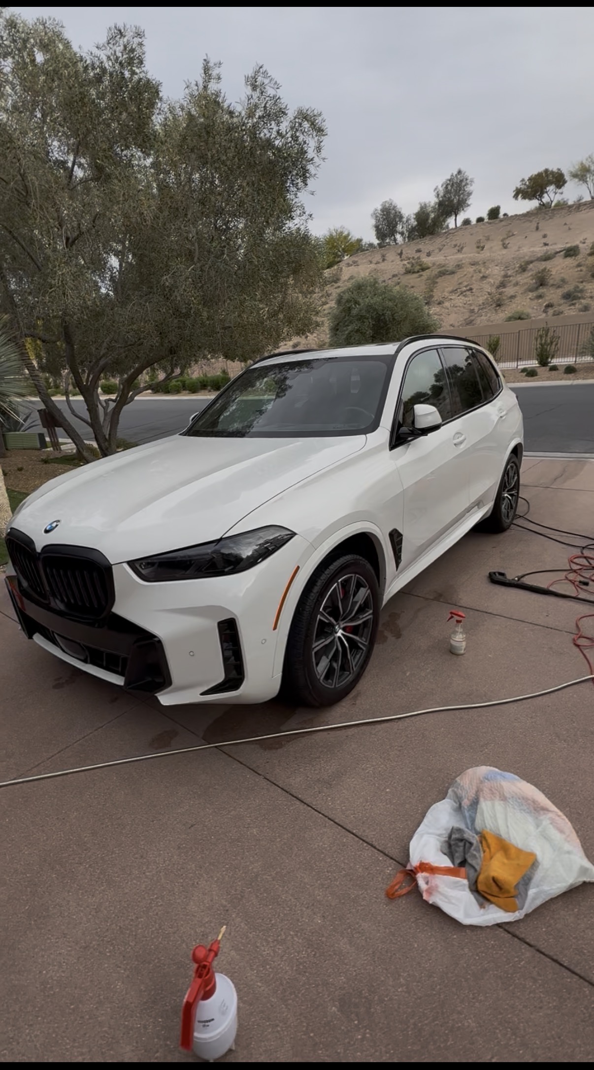 White BMW X5 detailed in driveway with cleaning supplies nearby