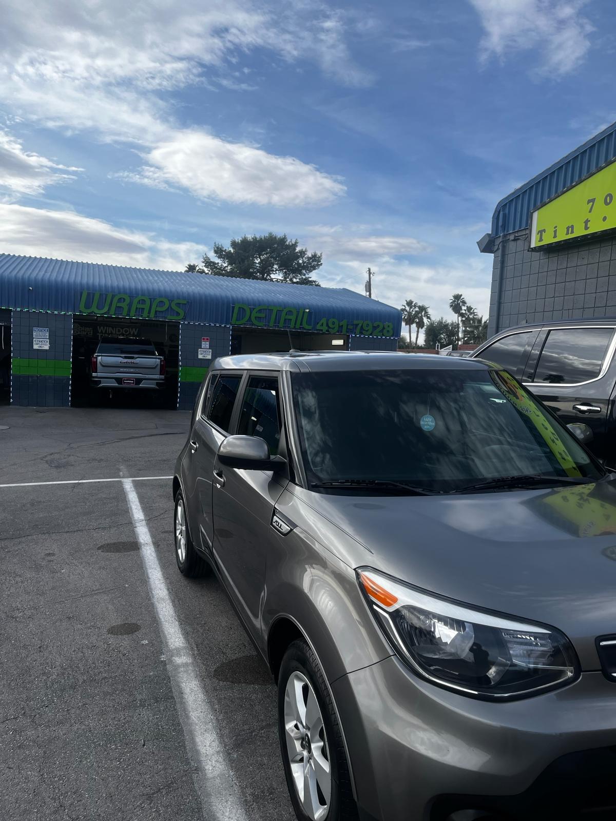 Gray Kia Soul parked outside shop with 'Wraps Detail 491-7928' signage
