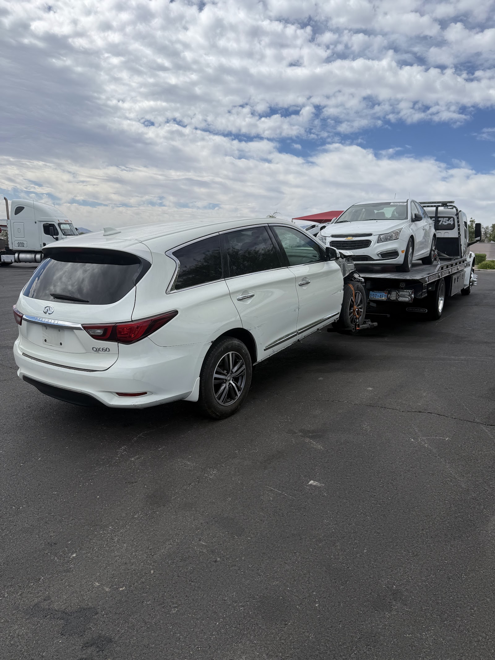 White Infiniti QX60 being loaded behind a flatbed carrying a damaged Chevrolet Cruze