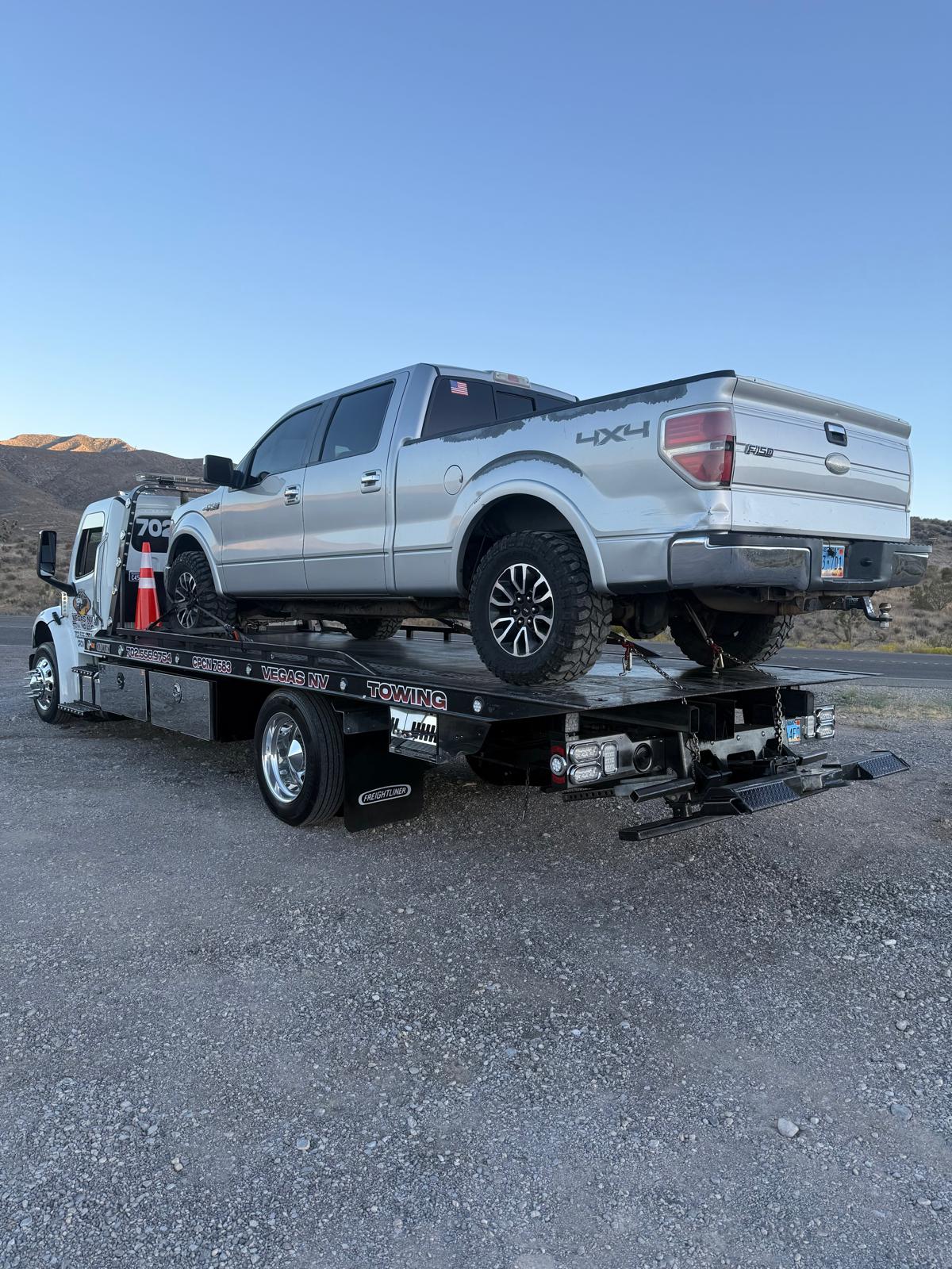 Silver Ford F-150 4x4 pickup on a Vegas NV Towing flatbed with desert mountains behind
