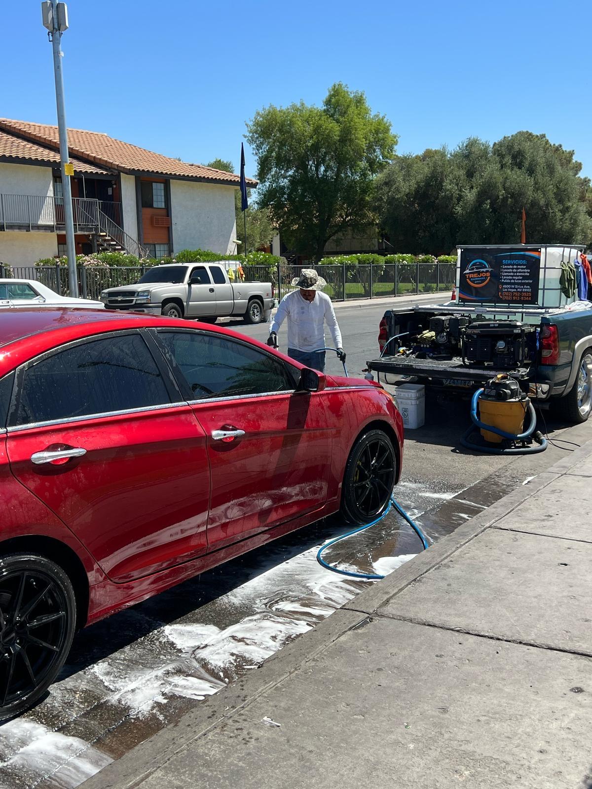Detailer washing a red sedan with mobile equipment truck in background