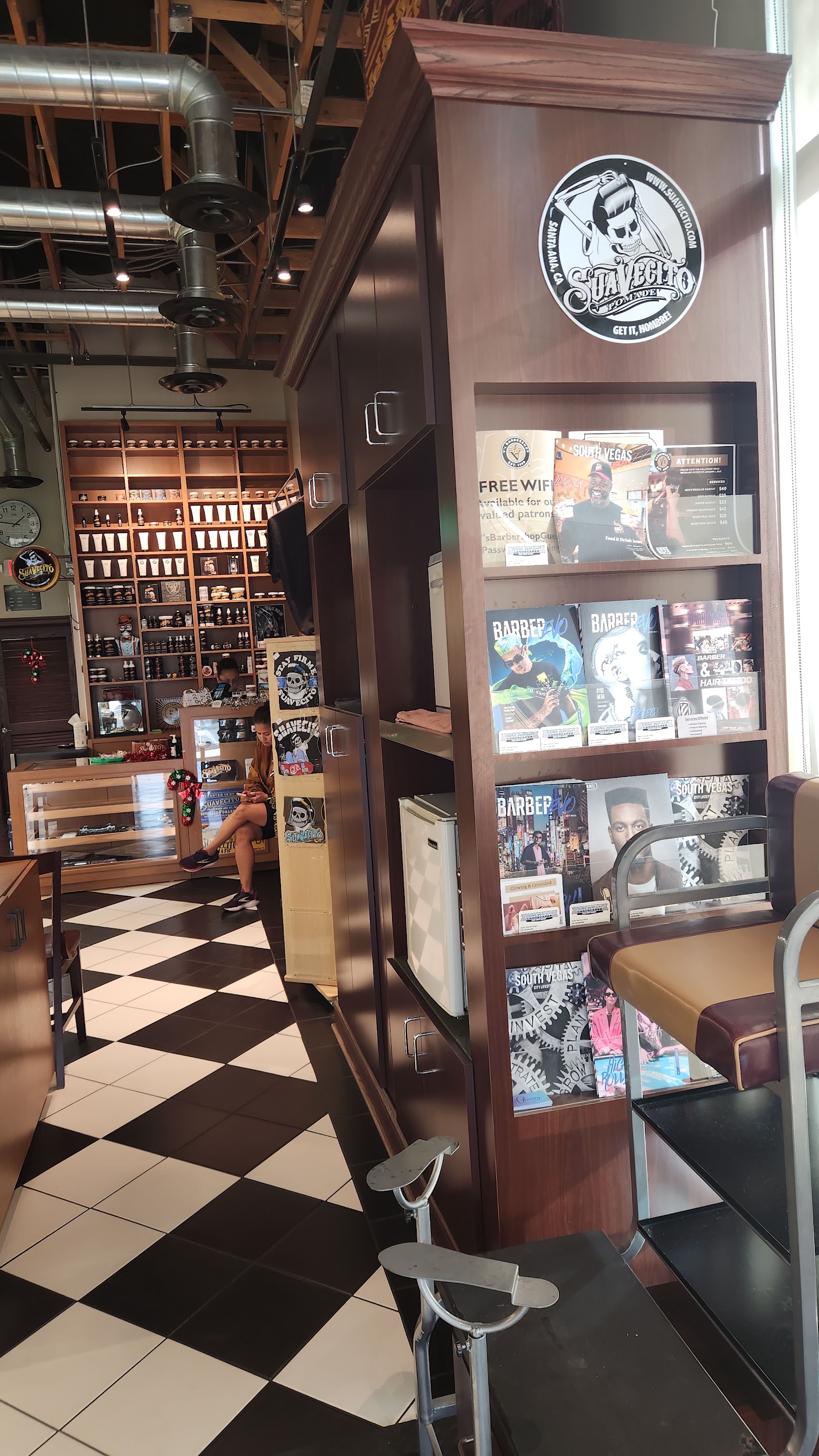 Barbershop interior showing product wall, magazine rack with Suavecito logo and checkered floor
