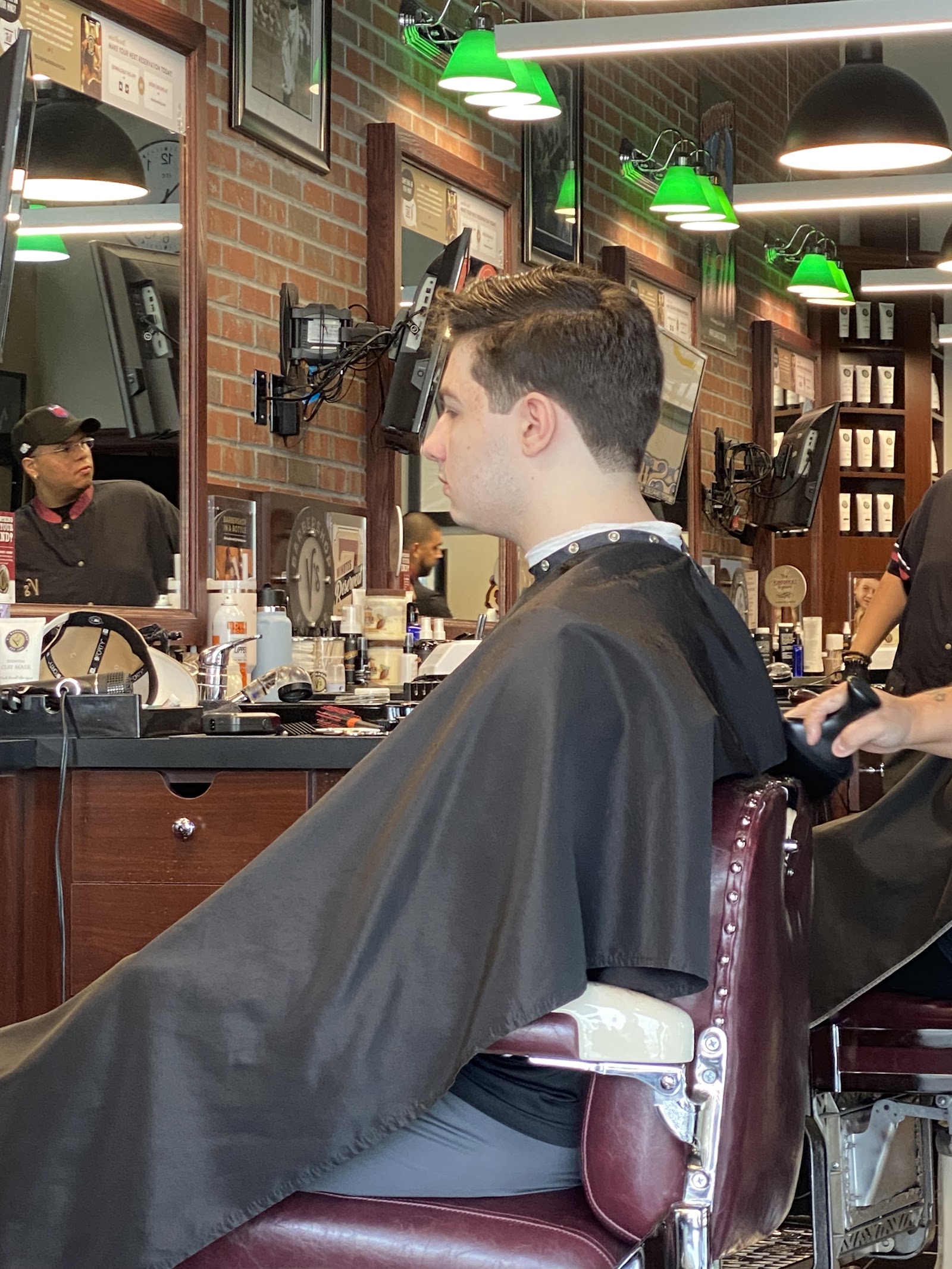 Client in barber chair with fresh cut, barbers and brick interior in background
