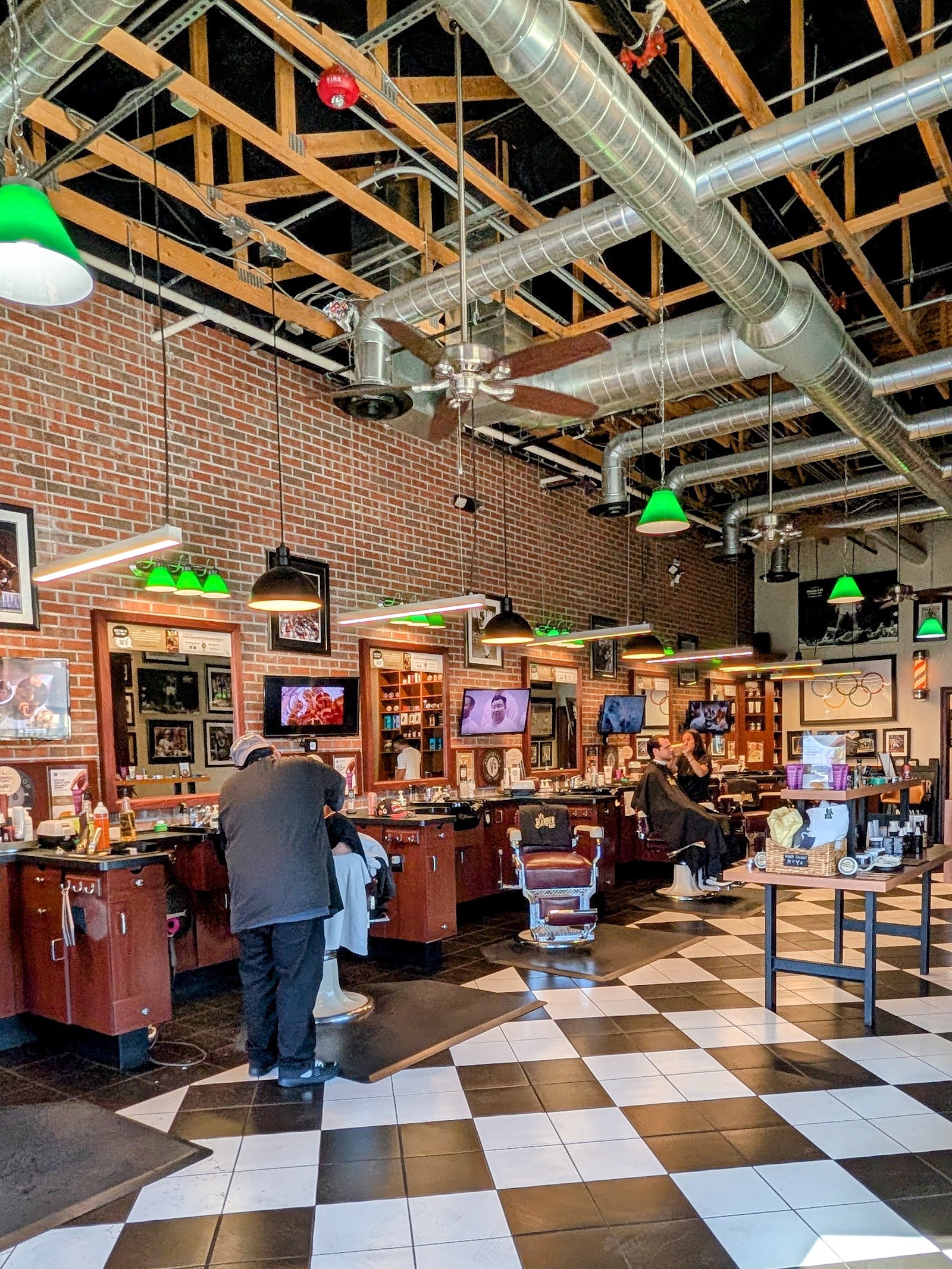 Spacious barbershop interior with exposed beams, brick walls, barber stations and checkered floor