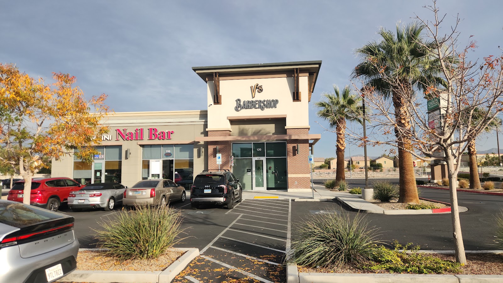 Exterior of V's Barbershop in a strip mall next to a Nail Bar with parking lot