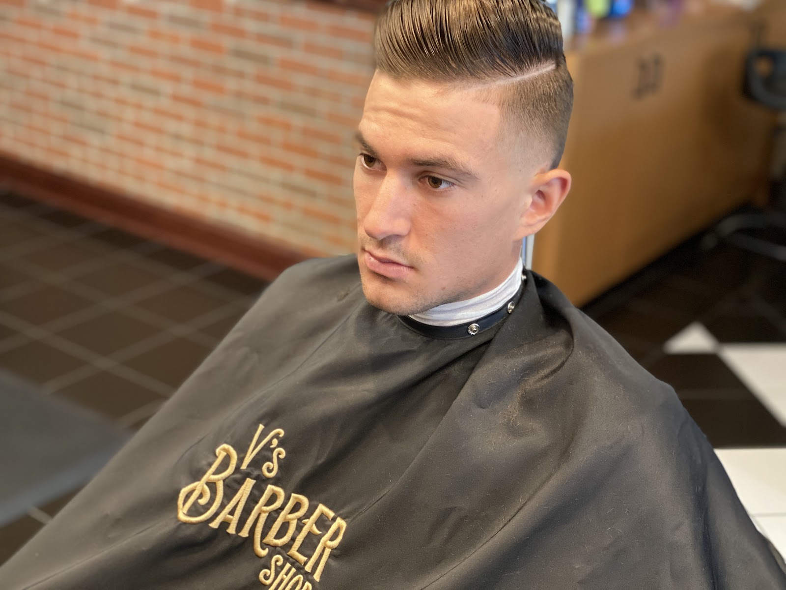 Close-up of man with sharp pompadour fade haircut wearing V's Barber Shop cape