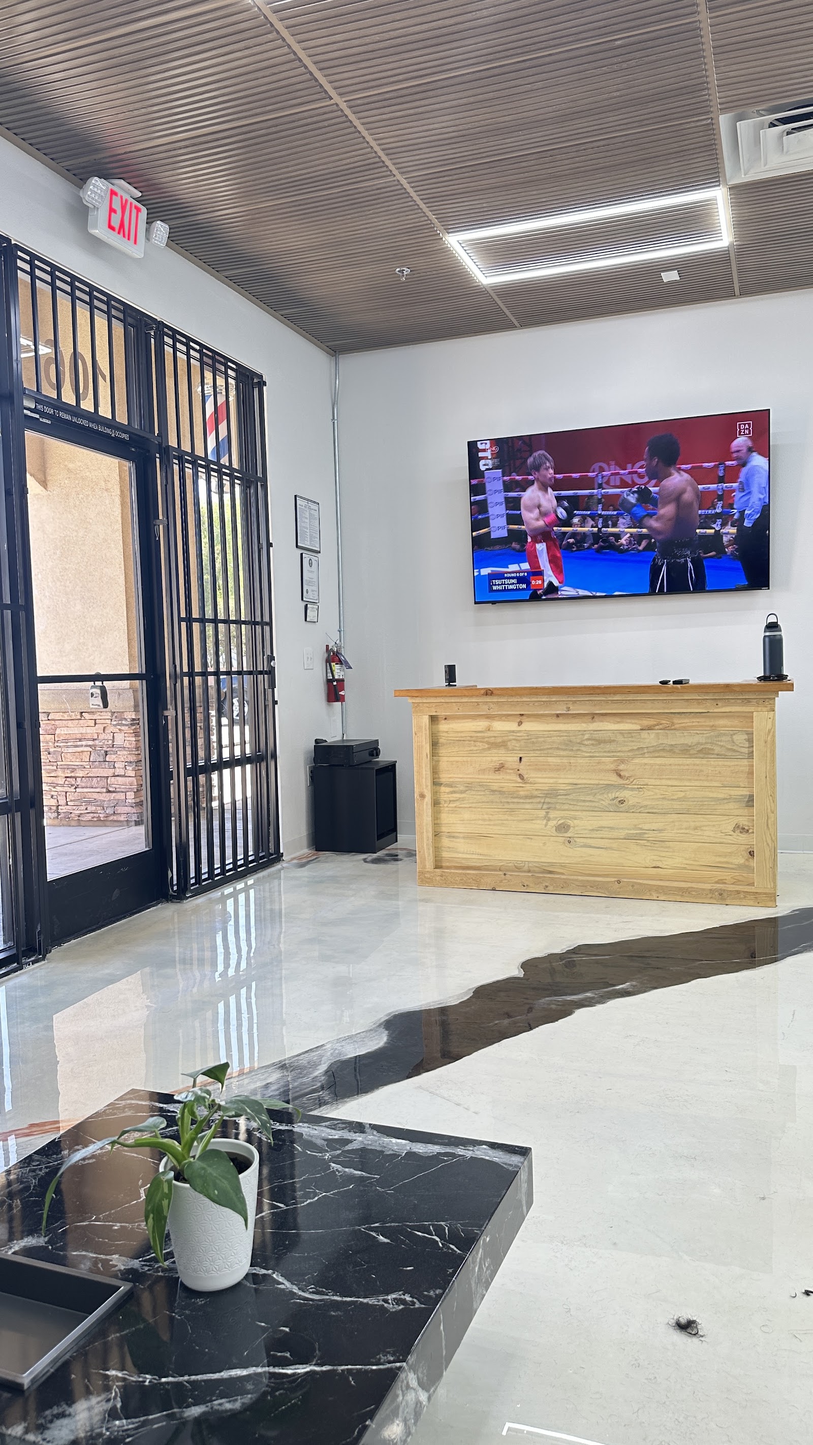 Barbershop waiting area with wood reception desk, wall-mounted TV, and entrance door